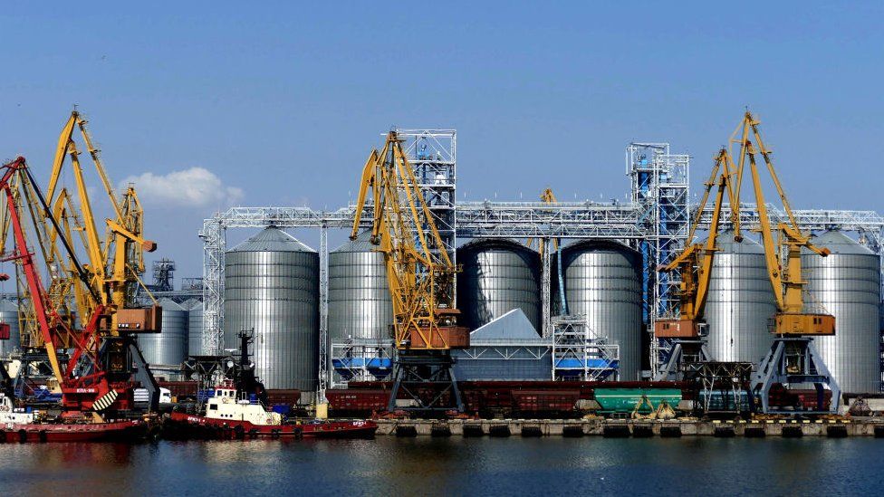 a ship is loaded with grain in front of silos at Odessa's port