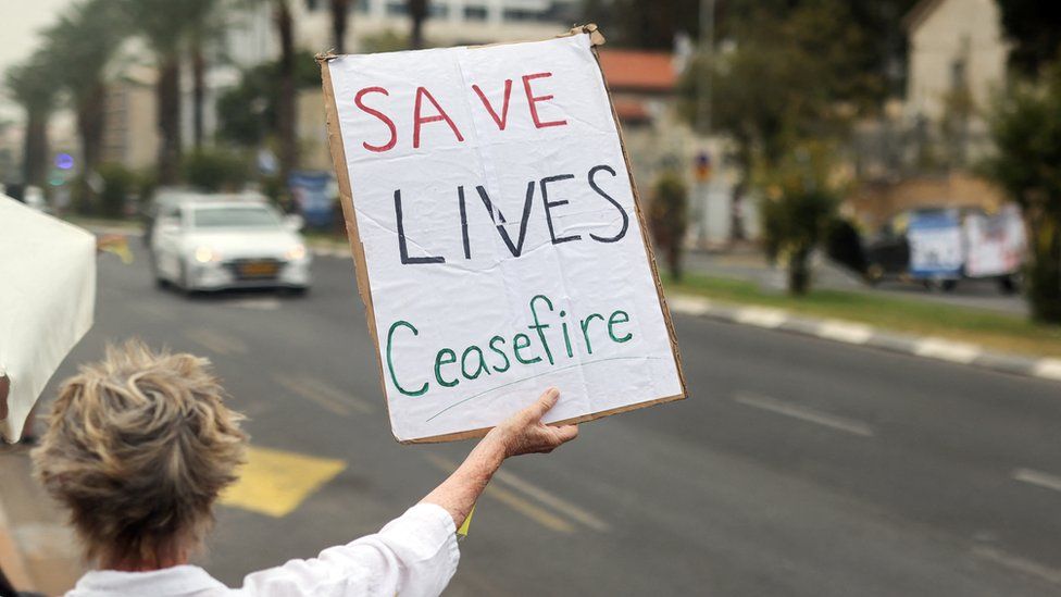 A woman holds a sign with the words "save lives, ceasefire" by the side of a road, in Tel Aviv, Israel.