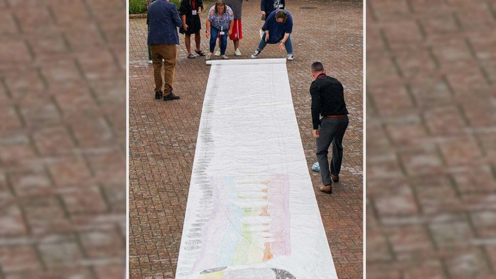 Harvey Price's train drawing being unrolled in a courtyard