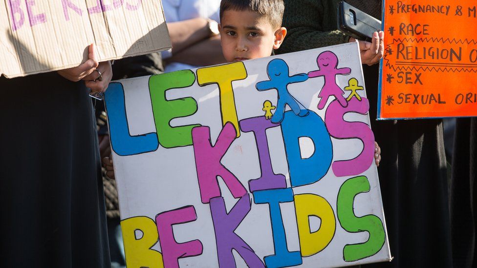 Child holding banner saying "Let kids be kids"