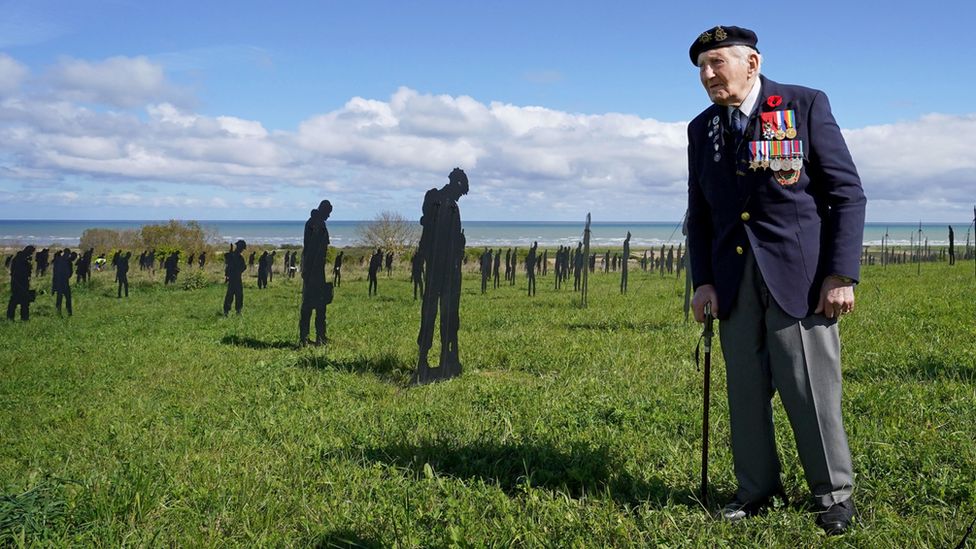 Veteran serviceman stands in front of silhouette figures