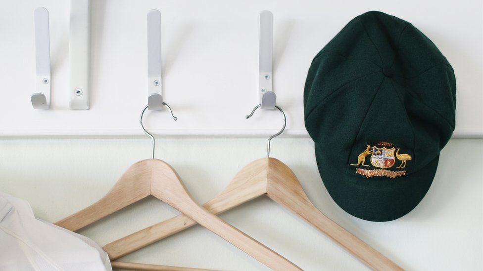 An Australian cricket cap hanging next to clothes hangers in a team dressing room