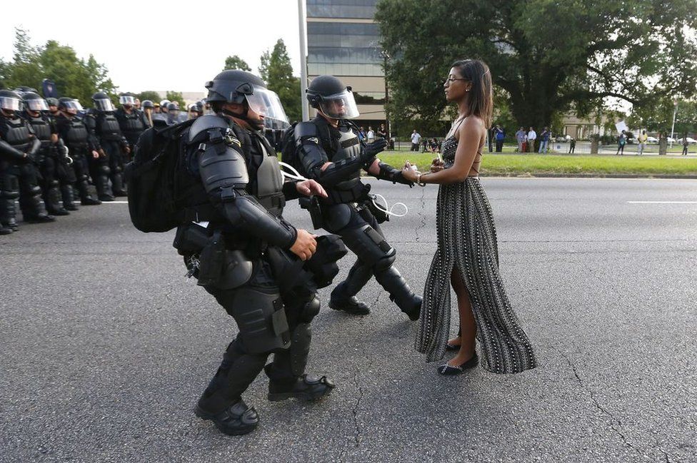 A woman stands in front of riot police