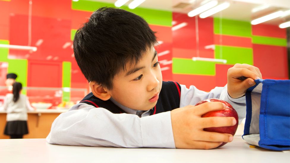 A Chinese student opens a lunch bag at a school cafeteria