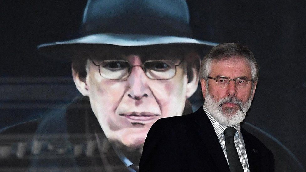 Gerry Adams walk past a portrait of former DUP leader Ian Paisley