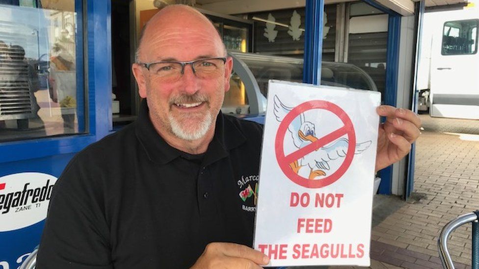 Owner of Marco's Cafe Marco Zeraschi with a sign asking customers to not feed the seagulls
