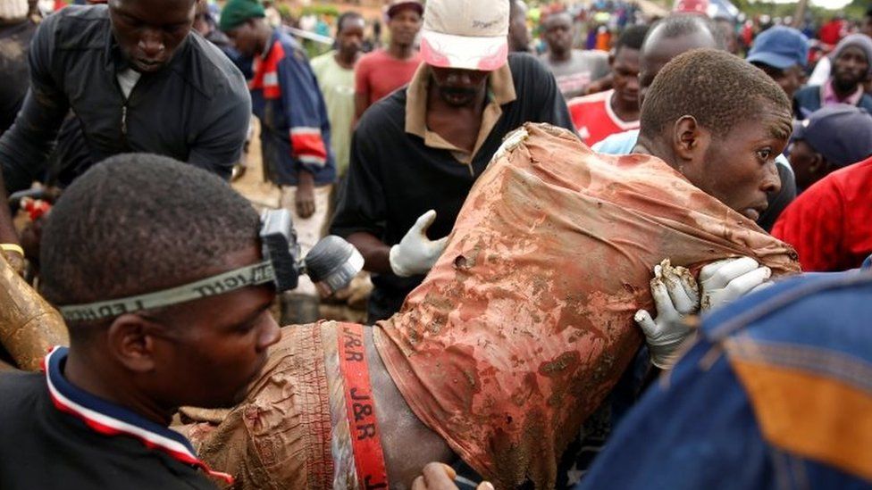A man being dragged out of a mine by many rescuers