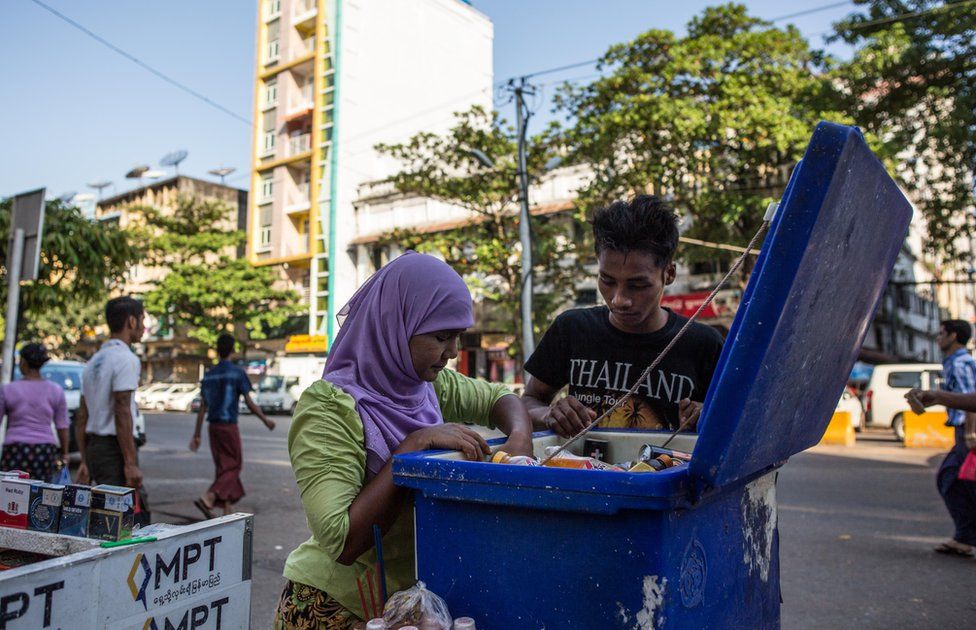 Thwarhairah assists a young man in looking for the right beverage in a cooler that she uses to supplement income from betel nut sales in downtown Yangon, Myanmar, November 14, 2015.