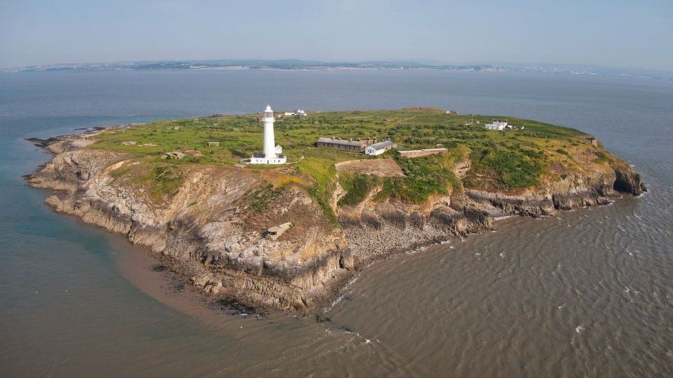 Flat Holm Island from above. The small green island has a five visible smallholdings and a large, white lighthouse.