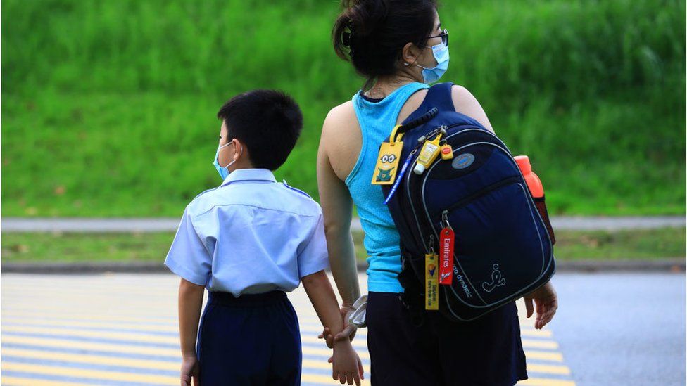 A woman walks a child to school donning the protective mask