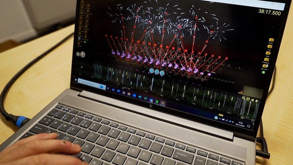 A hand on a laptop displaying a computer simulation of fireworks.