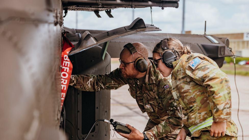 Two soldiers working on an Apache helicopter.