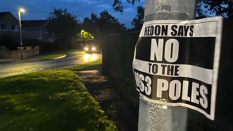 A sign, attached to a lamppost, says "Hedon Says No To The Pole"