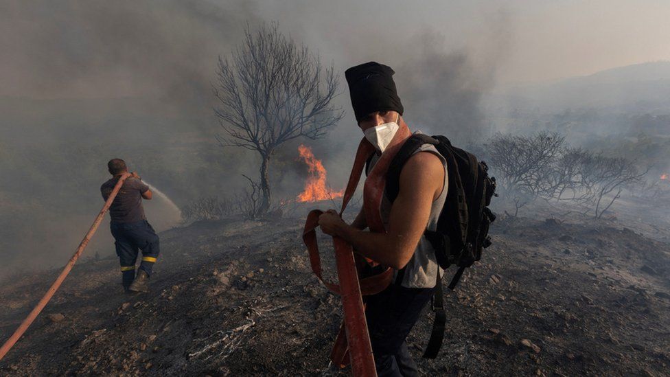 Firefighter Nektarios Kefalas and a volunteer try to extinguish a wildfire burning near the village of Asklipieio, on the island of Rhodes