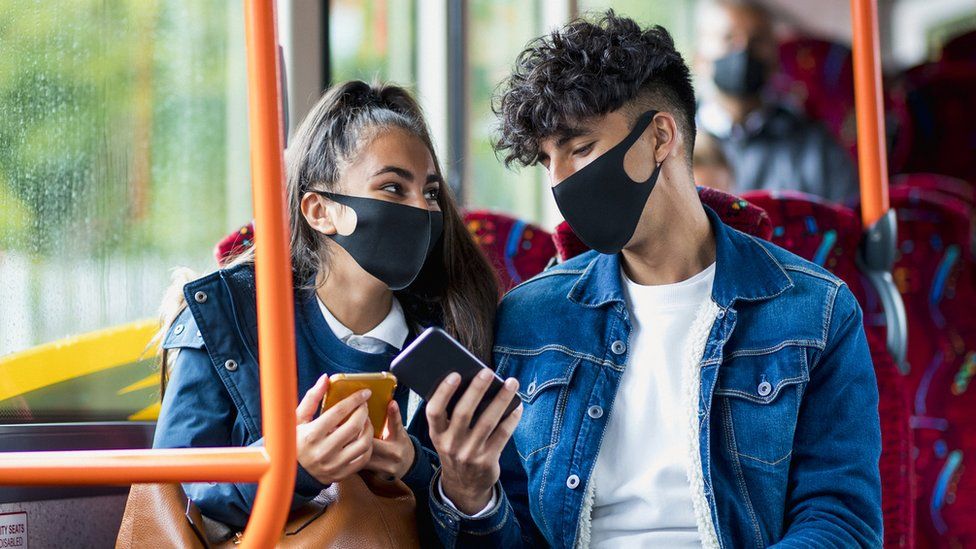 A man and a woman on the bus wearing face masks