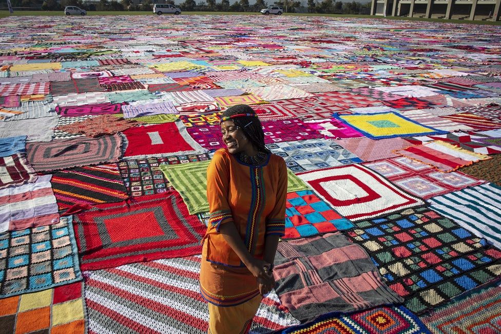 A performer stands in front of the thousands of knitted blankets on the school field at Steyn City to mark the upcoming Nelson Mandela Day as part of the 67 Blankets for Nelson Mandela Day project in Johannesburg, South Africa, 11 May 2021. The project sees thousands of blankets being knitted by "knitwits" and then given to those who need them during the cold winter in South Africa.