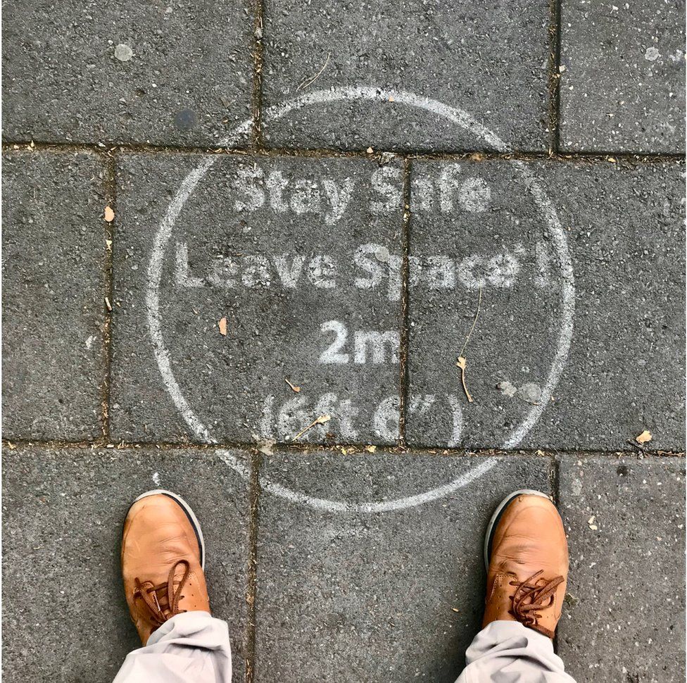A stencil outline instructing people to maintain a two-metre distance