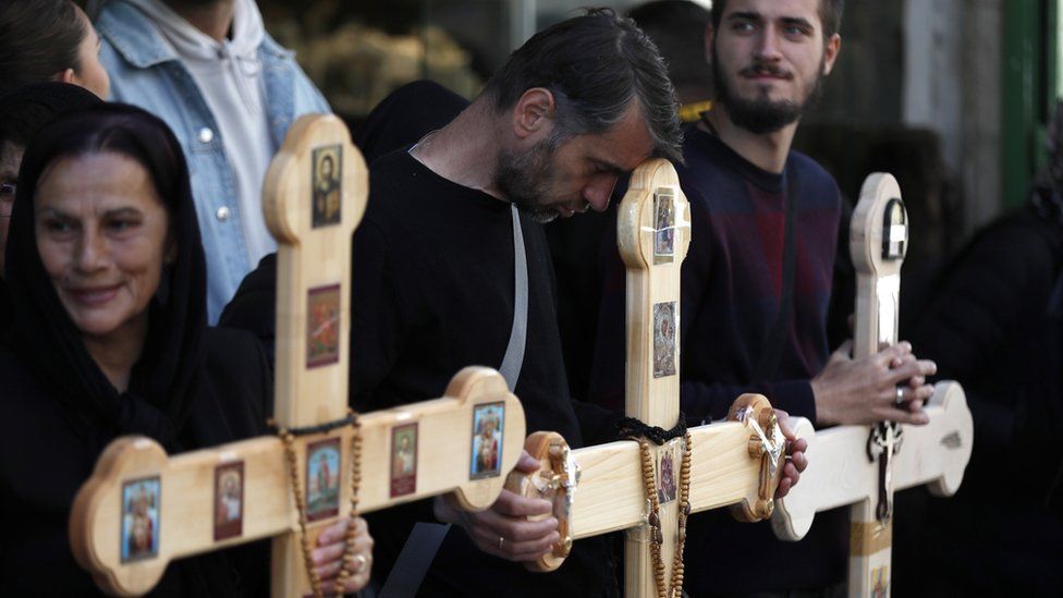 A Christian Orthodox pilgrim leans his head on a cross during a Good Friday procession