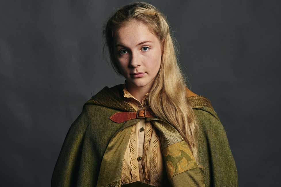 A woman with blonde hair wearing a green cloak