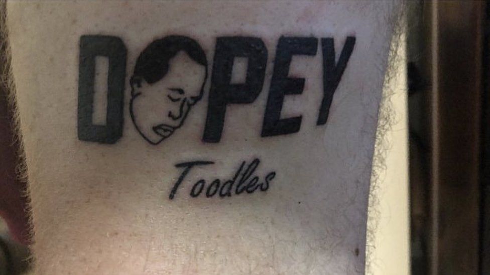 A Dopey logo tattoo, with the word 'toodles', on an unknown person's arm