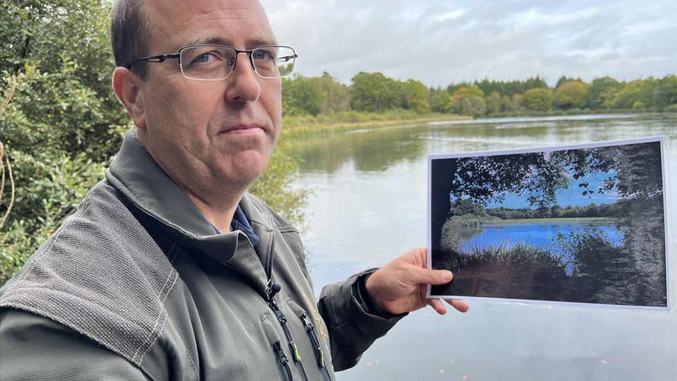 Rob Ballard holding picture in front of water with trees in the background