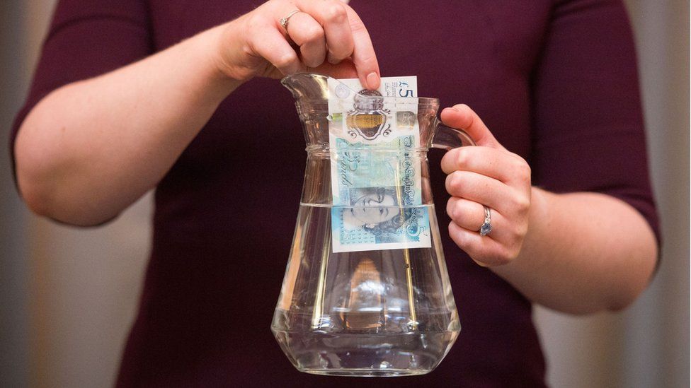 A woman dips a polymer £5 into a jug of water