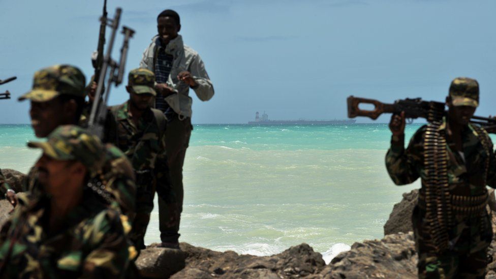 Armed militiamen and a pirate walk on a rocky outcrop on the coast in the central Somali