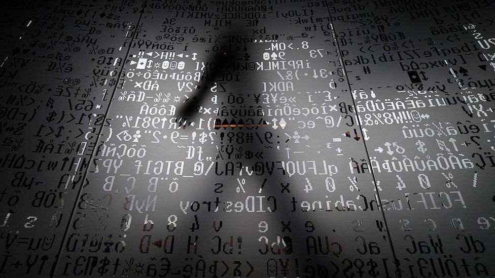 File photo showing a person walking behind a glass wall bearing machine coding symbols (17 October 2016)