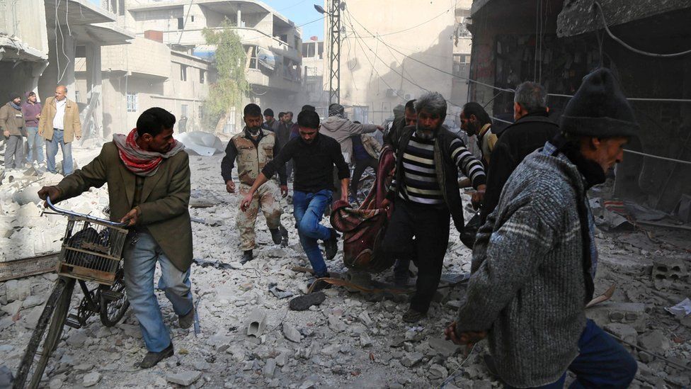 Syrian men carry a body in a blanket after a reported air strike in rebel-controlled Hamouria, in the Eastern Ghouta region outside Damascus (3 December 2017)