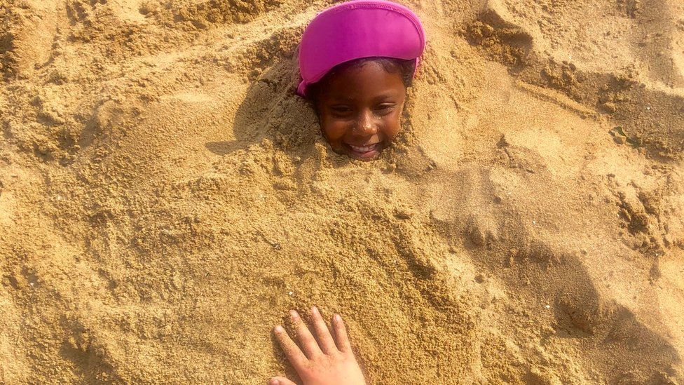 A girl smiles as she is partially buried on an excursion to a beach in Broadstairs, Kent