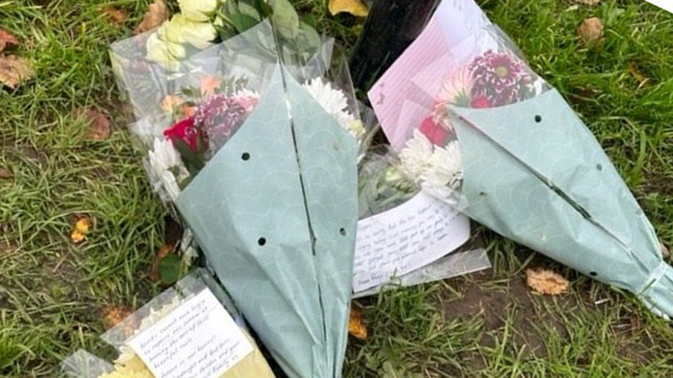 A small pile of flowers and handwritten notes lying on the ground near the scene of the fire