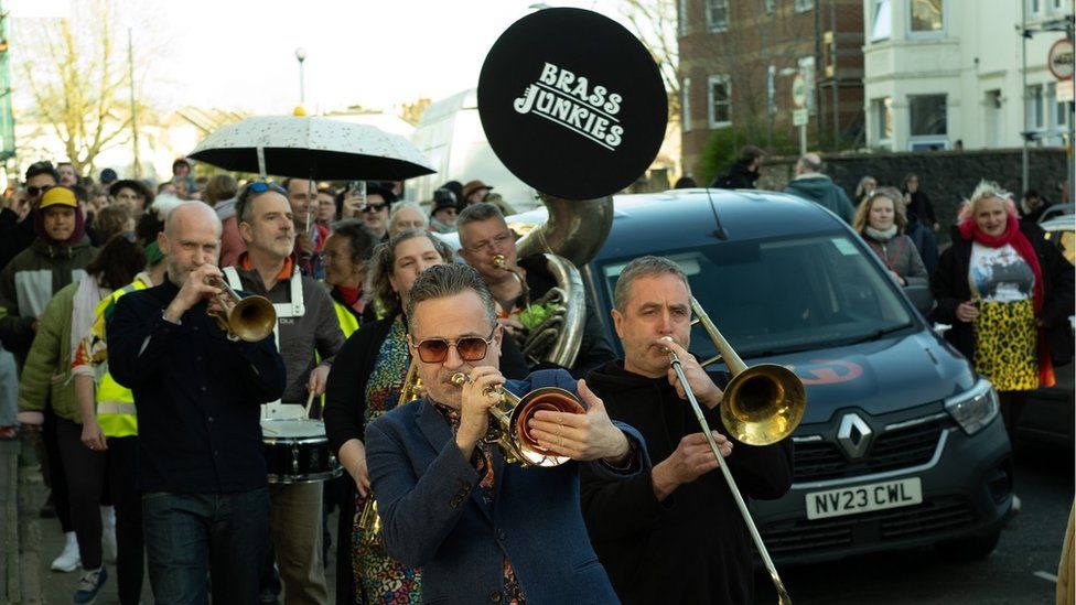 People walk along the street playing brass instruments at the start of the Bristol Jazz Festival