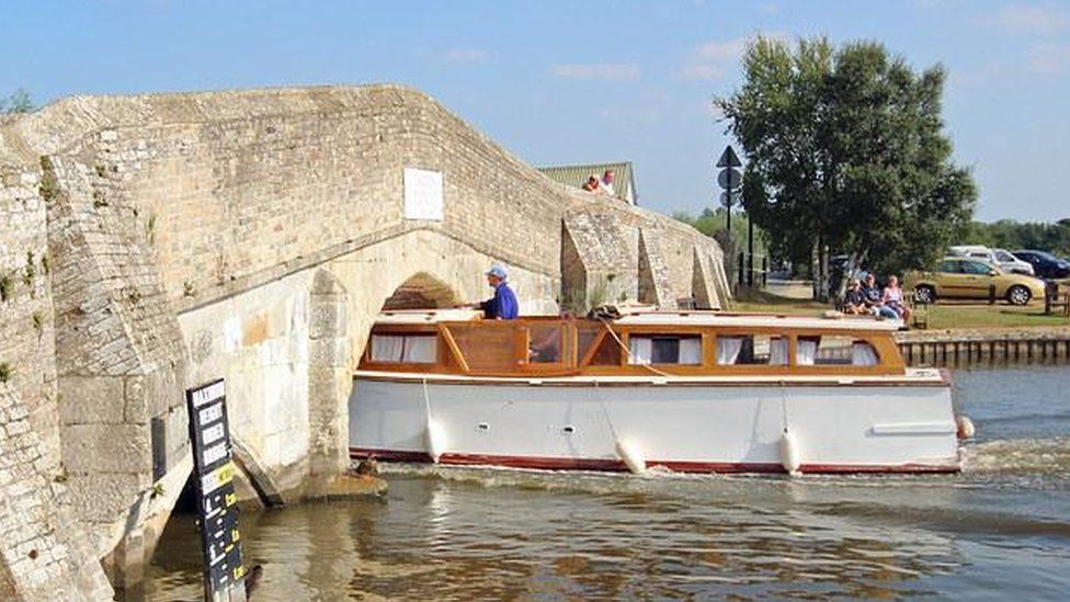 White and orange narrowboat being steered through a stone bridge