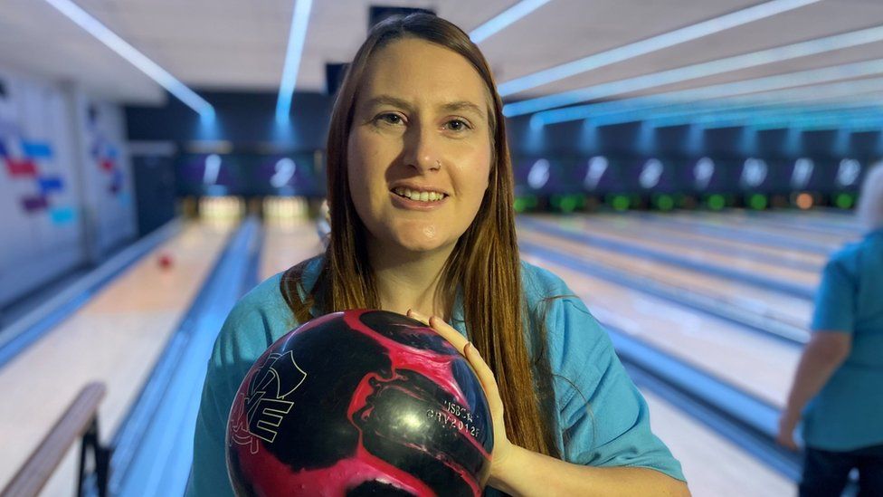 Bekcy Harrison standing in front of a bowling lane holding a pink bowling bowl towards the camera