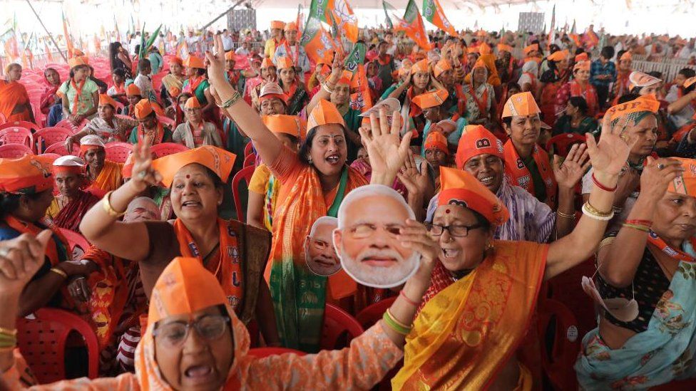 A crowd of BJP supporters cheer and wave paper signs of Prime Minister Modi's face