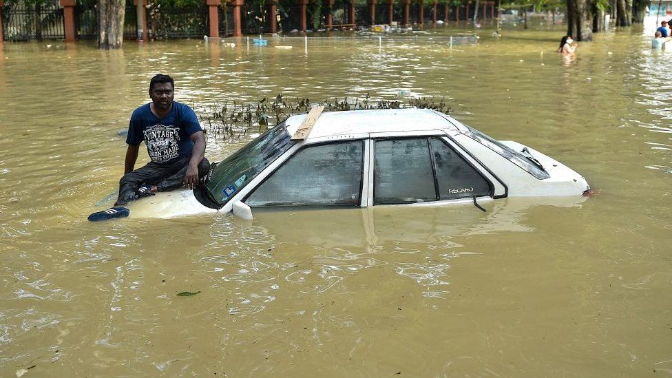 A man sits on the bonnet of a car as he waits to be evacuated by a rescue team in Shah Alam, Selangor on December 20, 2021, as Malaysia faces some of its worst floods for years.