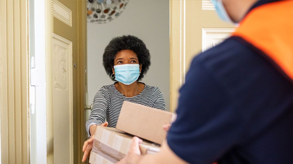 A stock image of a woman being handed a delivery at her front door