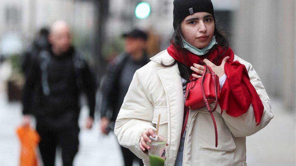 A woman with a mask under her chin walks along a shopping street