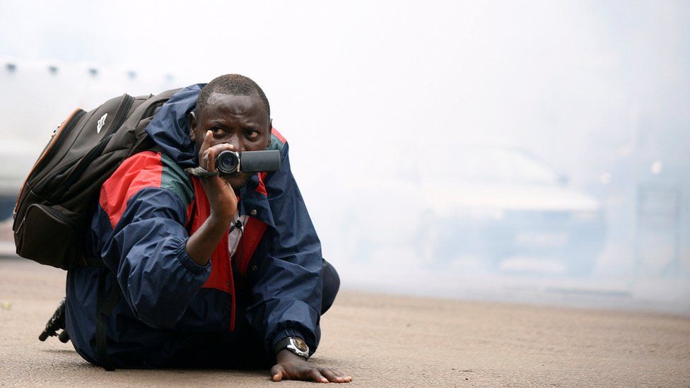 A Uganda journalists with his camera amid tear gas in Kampala, Uganda - Wednesday 11 July 2018