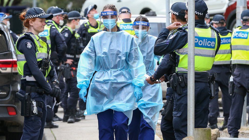Medical staff wearing protective equipment walk through a police guard