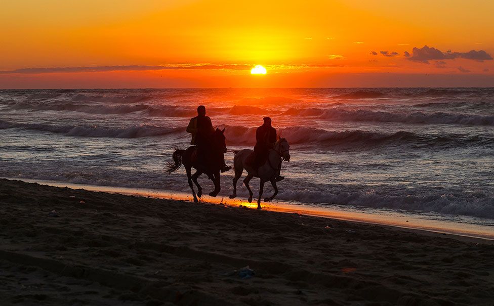 Palestinians ride horses at sunset along a beach in Gaza City