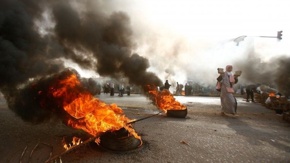 A protesters with pave stones walks past burning tyres in Khartoum, Sudan. Photo: 3 June 2019