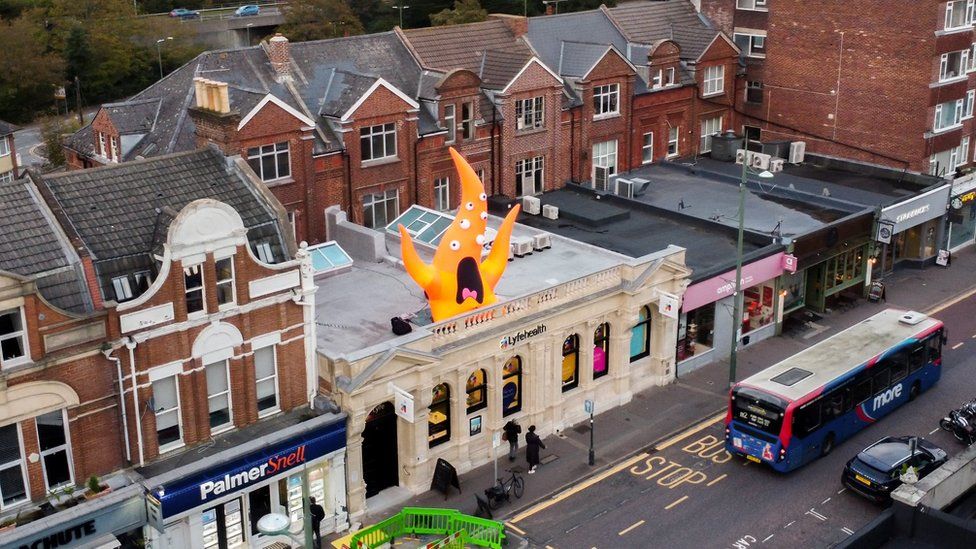 Aerial view of orange inflatable monster on top of a building in Westbourne