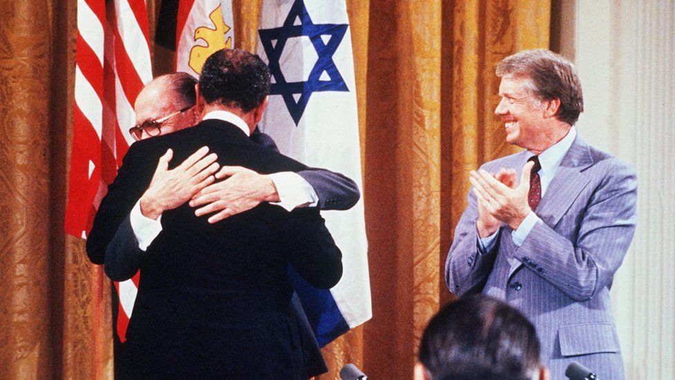 Israel's Menachem Begin and Egypt's Anwar Sadat (from behind) hug, as US President Jimmy Carter applauds (18 Sept 1978)