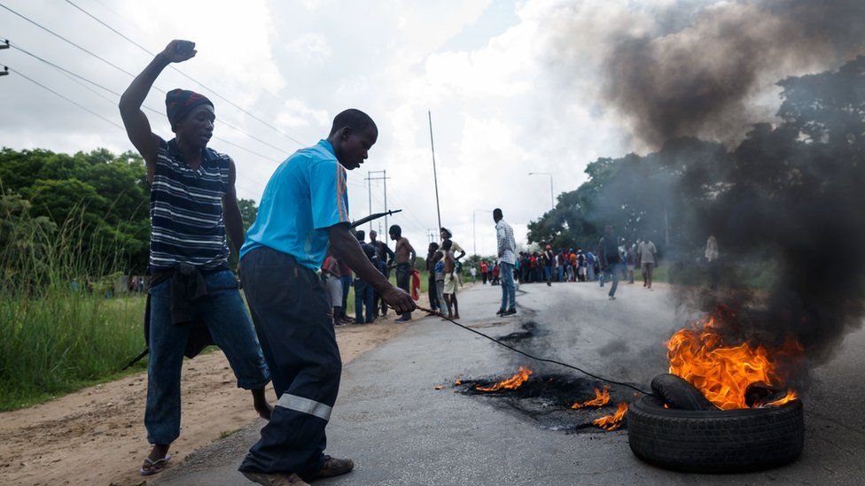 A man sets tyre on fire as angry protesters barricade the main route to Zimbabwe's capital Harare from Epworth township