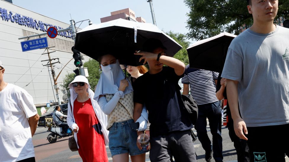 Люди прикрывают себя зонтиками и масками для лица от солнца на фоне оранжевого предупреждения о сильной жаре в Пекине 22 июня