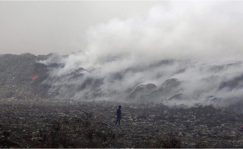 A boy stands amid garbage as smoke billows from the burning Deonar dumping ground in Mumbai in March 2016