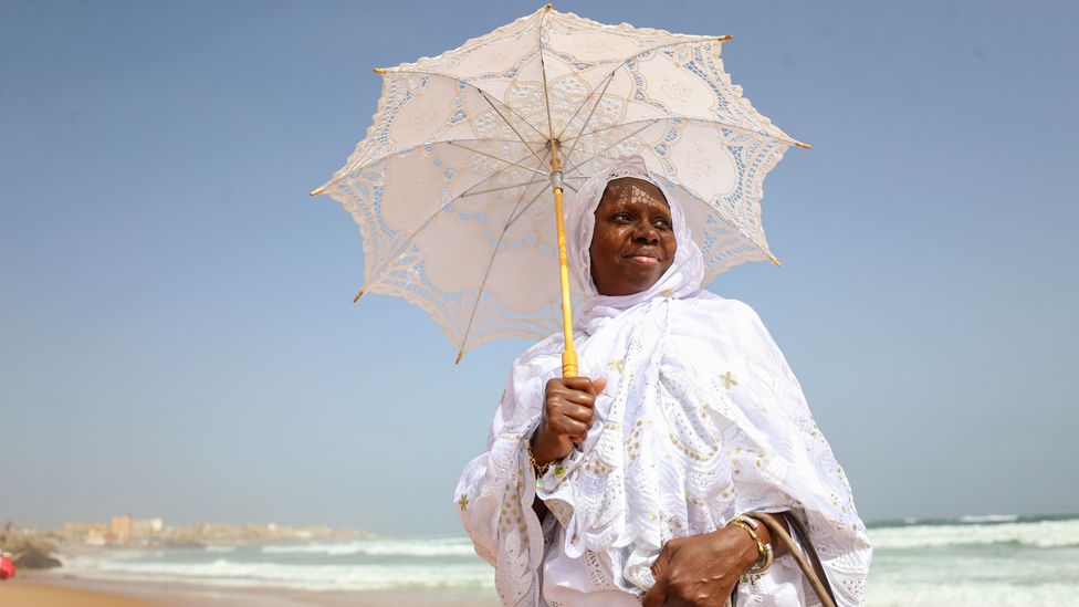 A woman with an umbrella dressed in white for Eid prayers on a beach in Dakar, Senegal - Wednesday 10 April 2024