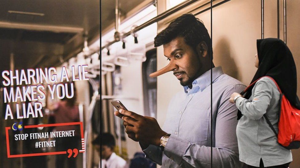 A commuter (R) walks past an advertisement reading 'sharing a lie makes u a liar' at a train station in Kuala Lumpur on March 26, 2018