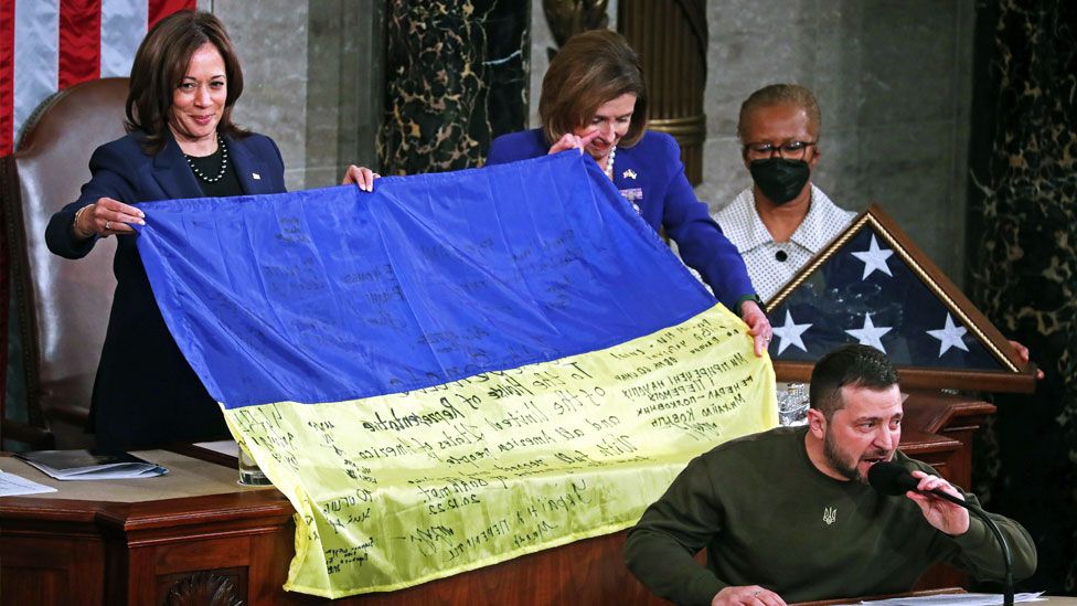Speaker of the House Nancy Pelosi (C) and US Vice President Kamala Harris (L) hold a Ukrainian flag after Ukrainian President Volodymyr Zelensky delivered an address to a joint meeting of the United States Congress in the House of Representatives chamber on Capitol Hill in Washington DC, USA, 21 December 2022